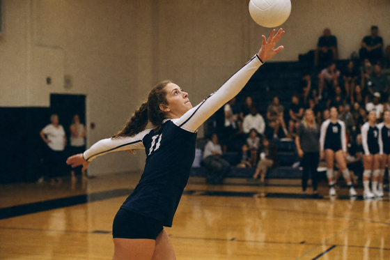 High school volleyball player at peak serve in a gym